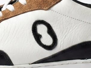 The Orate house mark, stitched in suede onto the quarter